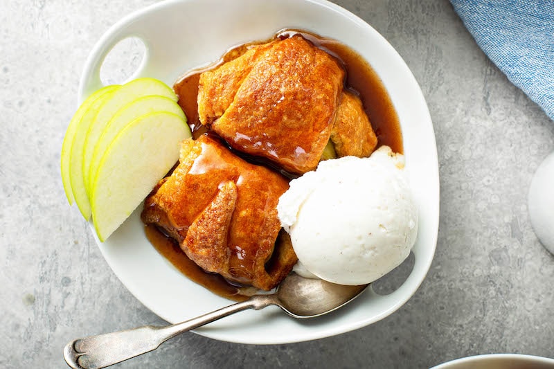 Two dumplings in a bowl with vanilla ice cream and apple slices.