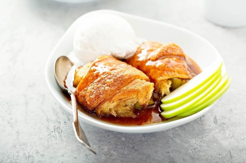 Two large apple dumplings with cinnamon sugar sauce in a bowl.