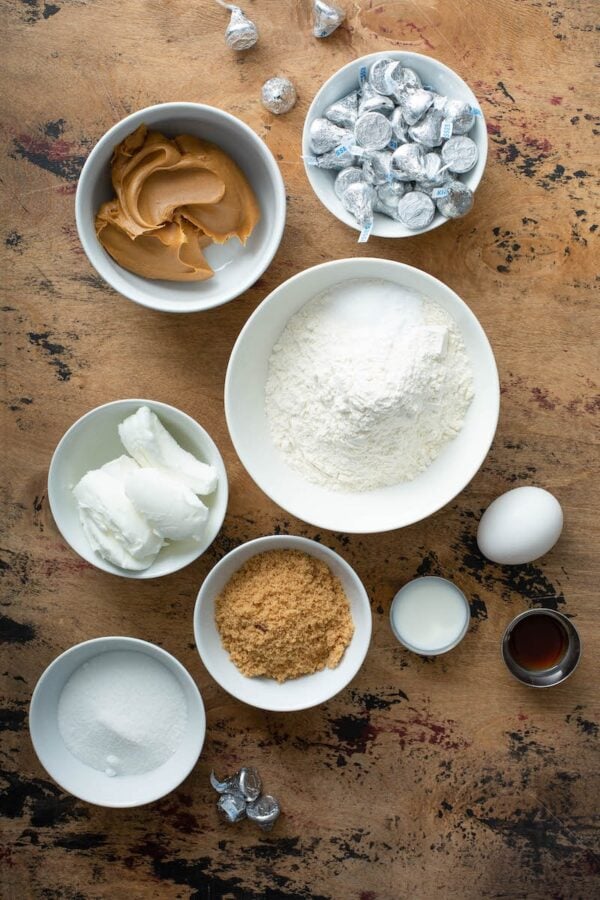 Peanut Butter Blossoms Ingredients in white bowls on a brown table top.