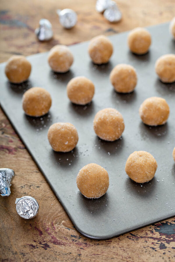 Peanut Butter Blossoms dough rolled into balls and sugar and then placed on a baking sheet.