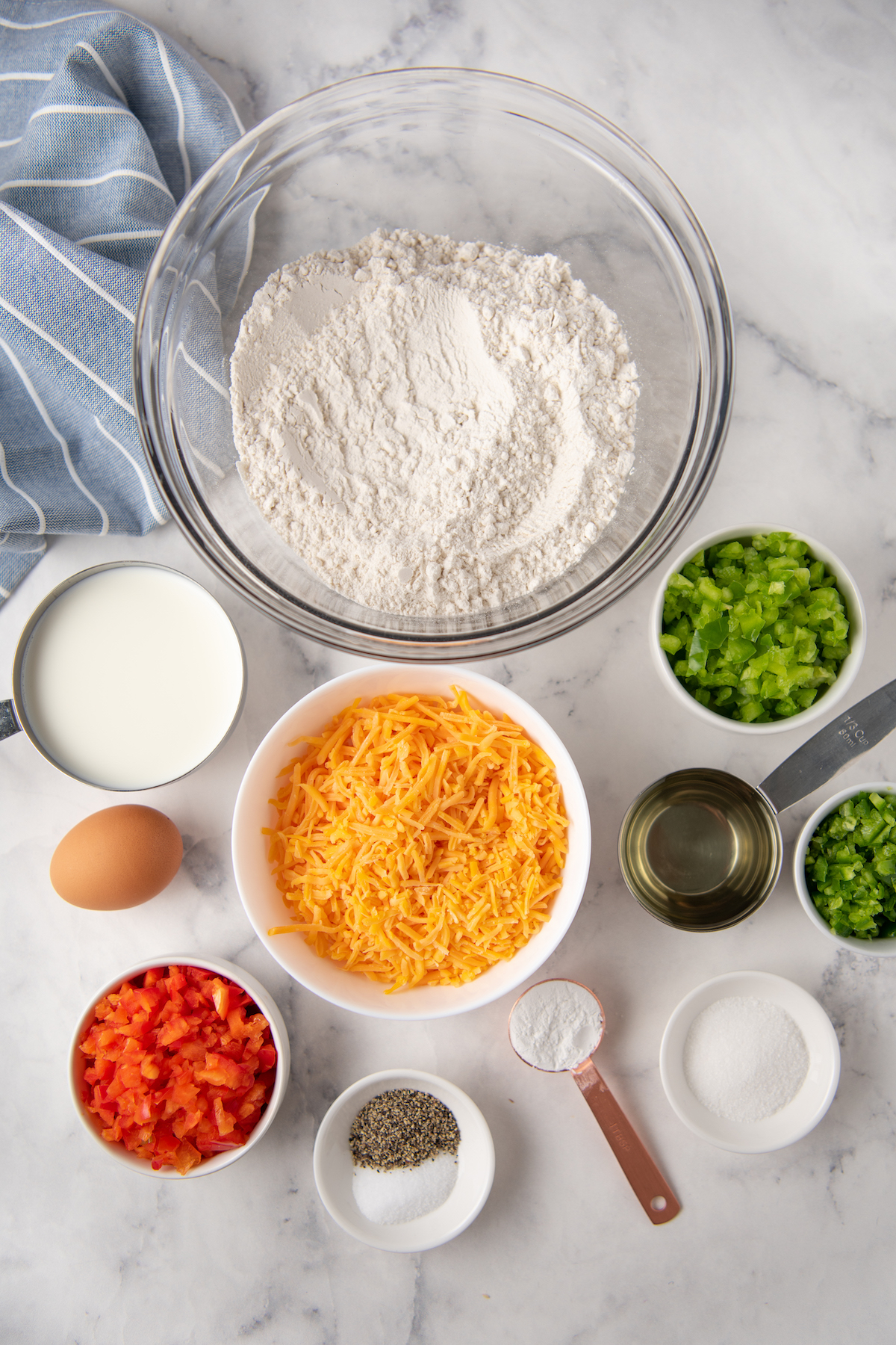From top: All-purpose flour, milk, cheddar cheese, diced green bell pepper, one egg, vegetable oil, diced jalapeno, diced red bell pepper, salt and black pepper, baking soda, salt.