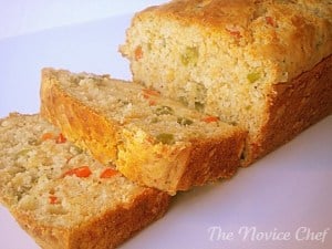 golden yellow bread loaf with two slices cut off on a white plate. Inside of bread showing red and green jalapeno pepper pieces.