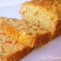 golden yellow bread loaf with two slices cut off on a white plate. Inside of bread showing red and green jalapeno pepper pieces.