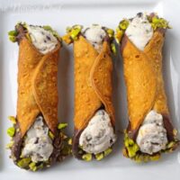 Three cannoli on a white plate with chocolate and pistachio on the ends.