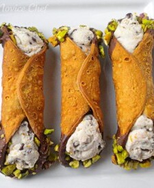 Three cannoli on a white plate with chocolate and pistachio on the ends.