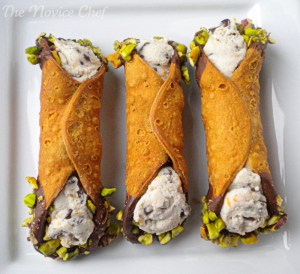 Three cannoli on a white plate with chocolate and pistachio on the ends.