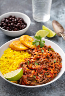 Ropa Vieja on a plate with rice, plantains and black beans.