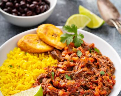 Ropa Vieja on a plate with rice, plantains and black beans.
