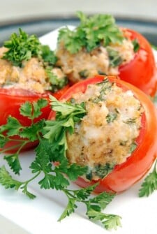 Close up view of three red tomatoes stuffed with cheese and breadcrumbs garnished with green parsley on a white plate