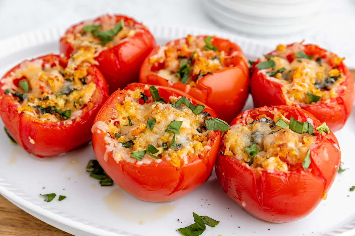 Baked tomatoes stuffed with cheese and breadcrumbs on a white plate with basil on top. 