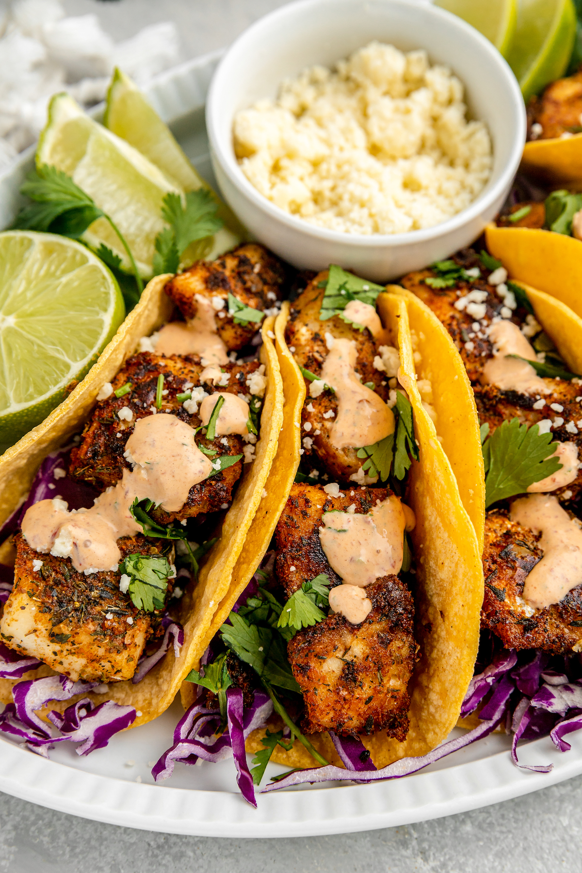 Blackened Fish Tacos on a platter with a cup of creamy cilantro-lime sauce and fresh lime wedges.