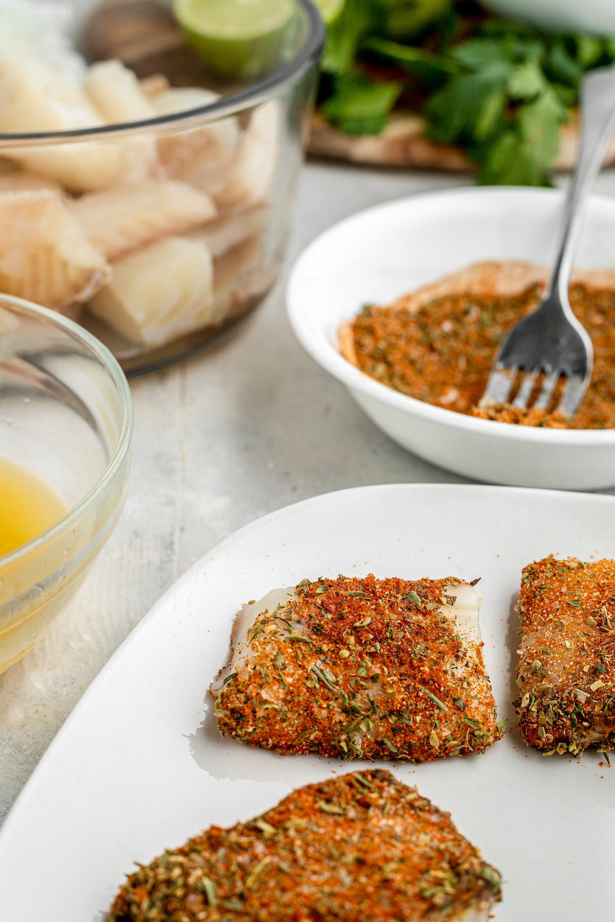 Fish fillets coated with spices on a plate with fish, butter, and spices in the background.
