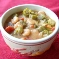 A white bowl with handles is filled with seafood gumbo