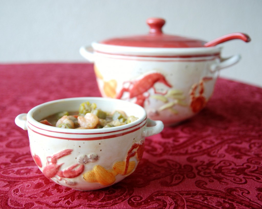 A decorative bowl with handles is filled with seafood gumbo