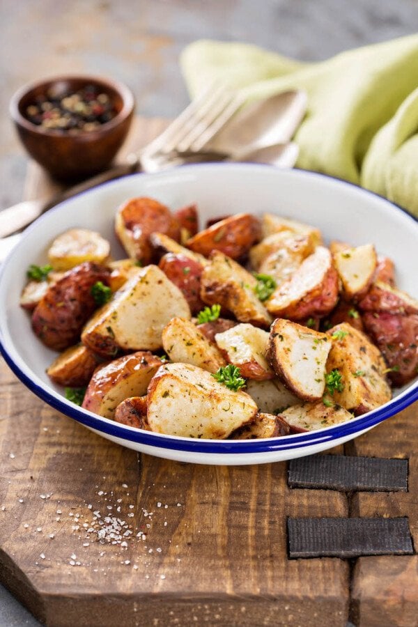 Roast potatoes in a white bowl on a cutting board.