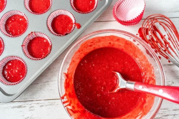 Red velvet cupcake batter next to a filled muffin tin.