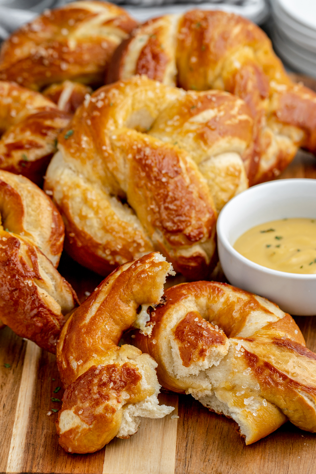 Pretzels piled around a small cup of dipping sauce. One pretzel is broken in half to show texture.