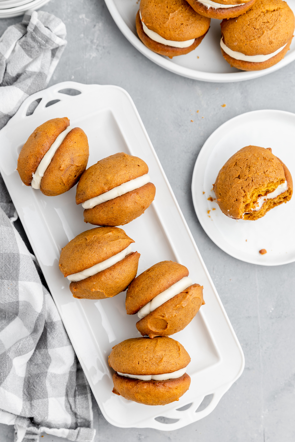 White serving plates with pumpkin whoopie pies arranged on them. One pie is on a small white dessert plate.