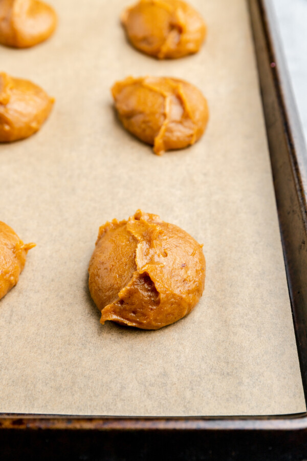 Rounds of unbaked pumpkin batter on a parchment-lined baking sheet.