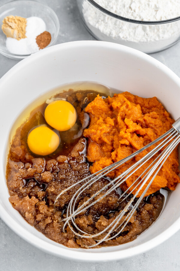 Brown sugar, eggs, pumpkin puree, and other ingredients in a mixing bowl with a whisk.