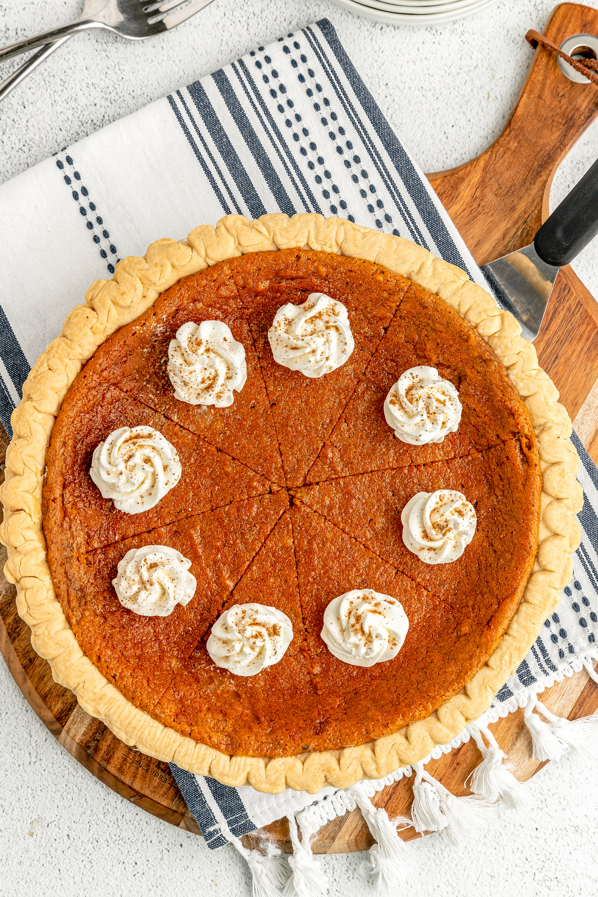 An overhead shot of a sweet potato buttermilk pie, cut into 8 slices and garnished with rosettes of whipped cream and cinnamon.