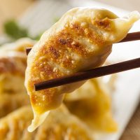 Chinese Dumpling (potsticker) being held with chopsticks.