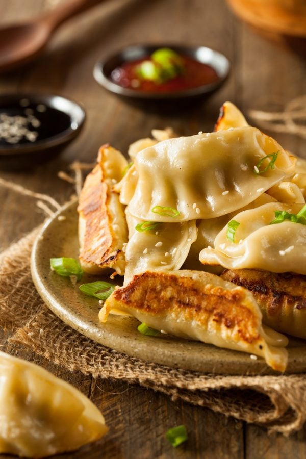 Potstickers on a plate with Potstickers sauce, scallions and sesame seeds on top. 