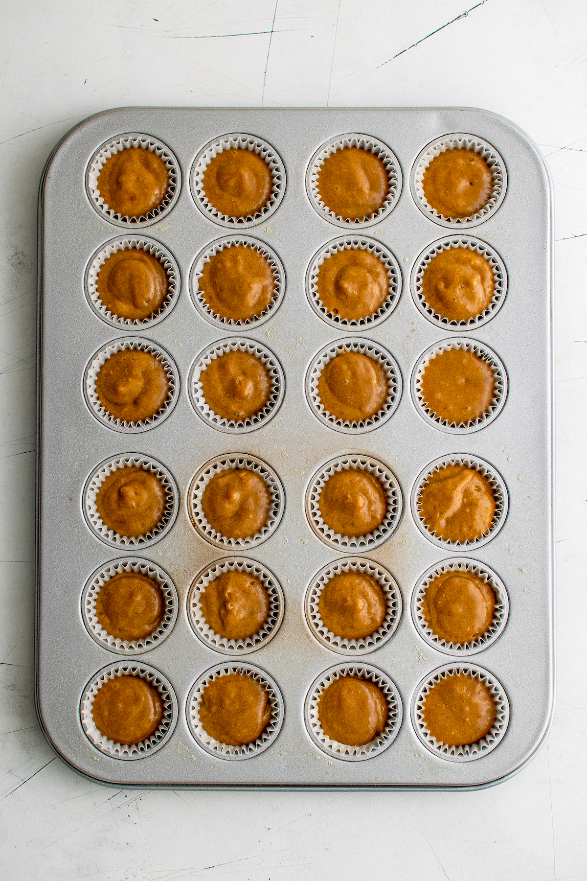 Overhead shot of a mini-muffin pan. Each well is lined with a paper liner, and each liner is almost full of unbaked batter.