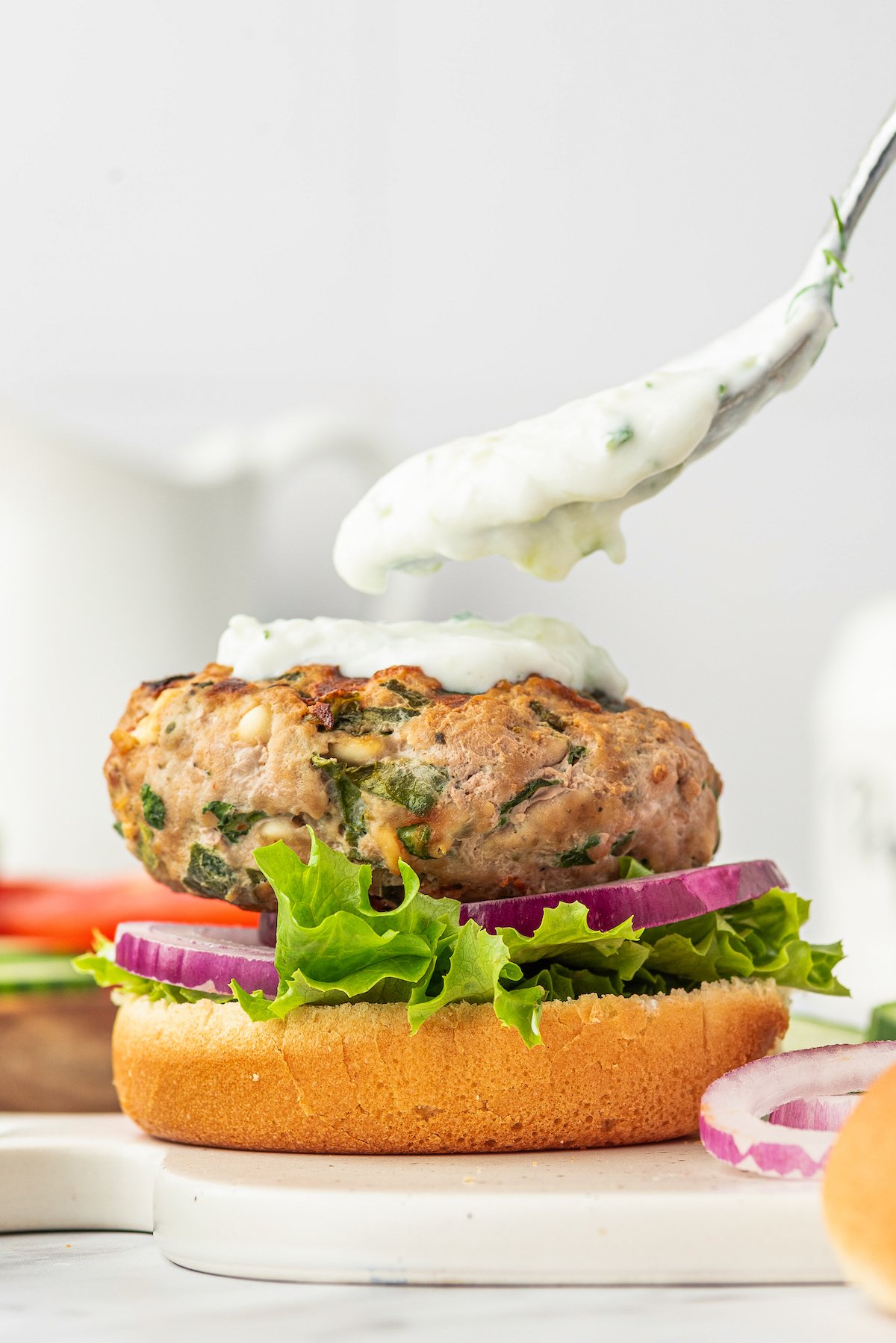 An open-faced turkey burger being topped with creamy sauce.