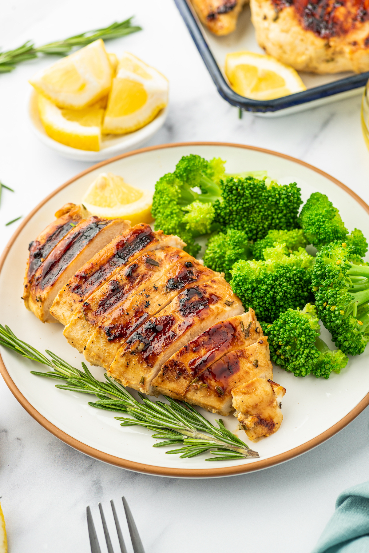Sliced grilled rosemary honey mustard chicken on a plate, with a side of steamed broccoli and a rosemary garnish.