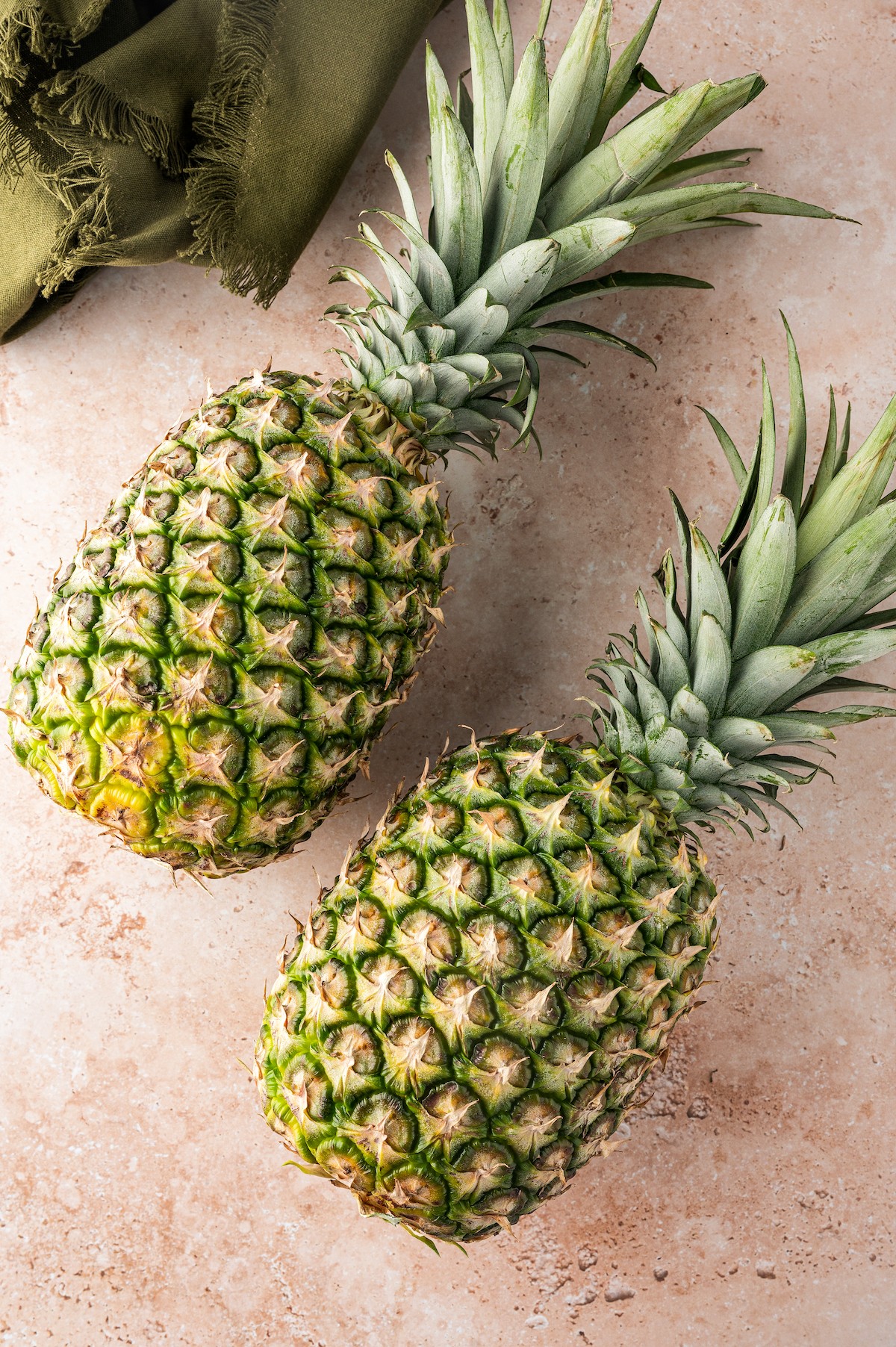 Two fresh pineapples laying side by side on a work surface.