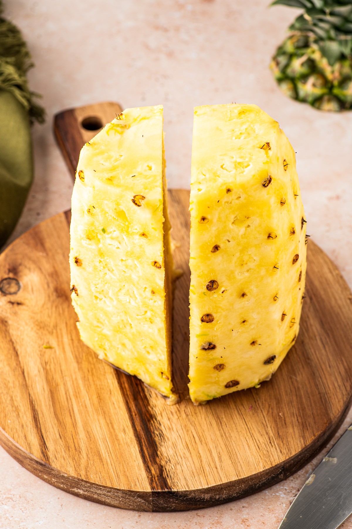 Cutting the pineapple in half from top to bottom.
