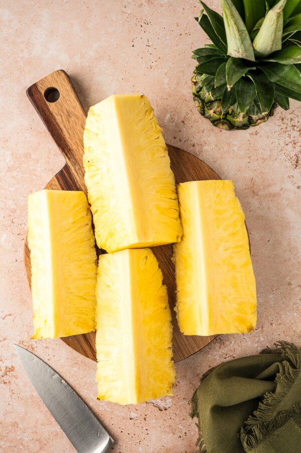 Four quarters of pineapple on a cutting board.