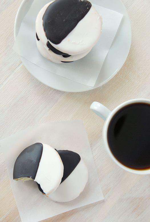 Two stacks of black and white cookies beside a cup of coffee