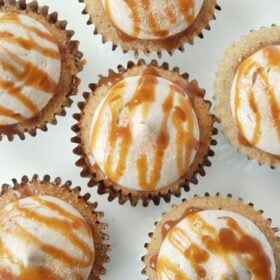 Six churro cupcakes with cream cheese frosting drizzled with caramel sauce on white plate