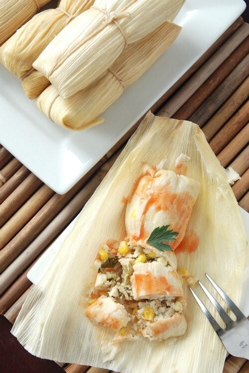 Overhead image of wrapped tamales and one tamale unwrapped.