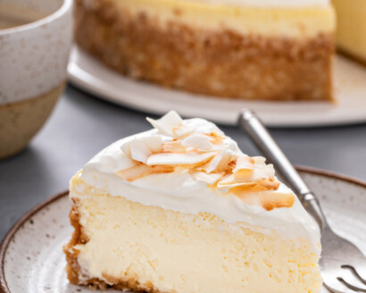 A slice of coconut cheesecake topped with whipped cream and toasted coconut.