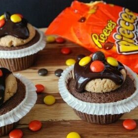 three cupcakes with candy on top and bag of candy behind