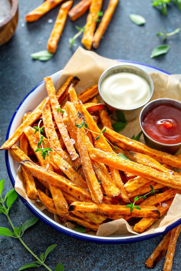 Bowl of baked sweet potato fries with two dipping sauces on the side. 