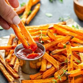 Sweet potato fries on parchment paper being dipped into ketchup.