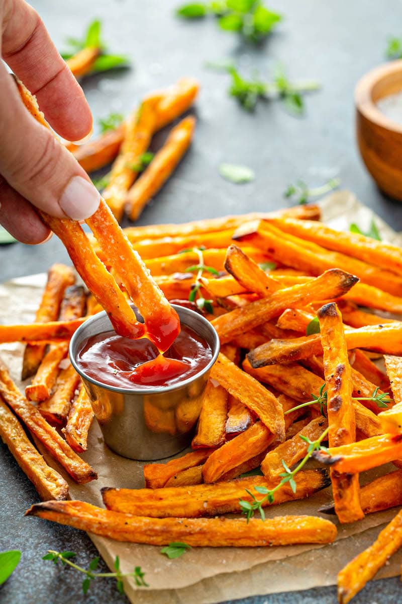 Sweet potato fries on parchment paper being dipped into ketchup. 