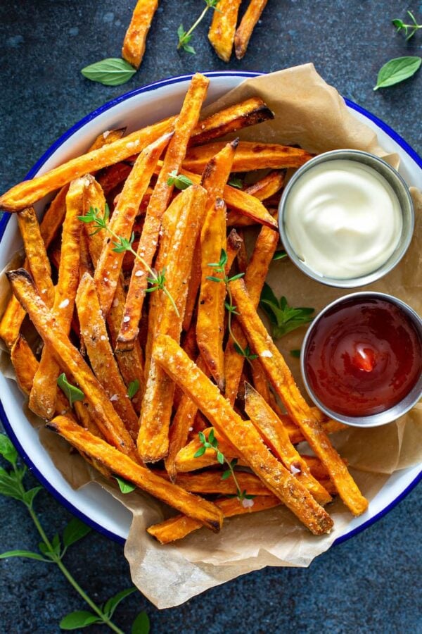 Bowl lined with parchment paper and filled with sweet potato fries and two dips. 