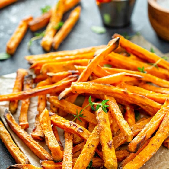 Sweet potato fries on parchment paper with herbs on top.