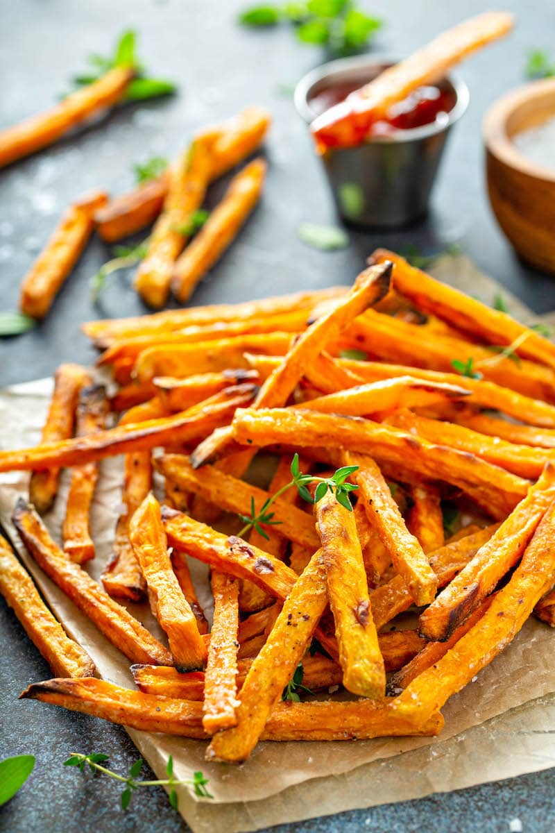 Sweet potato fries on parchment paper with herbs on top.