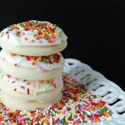 Four sugar cookies sitting on a plate of sprinkles stacked on top of each other.
