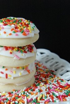 Four sugar cookies sitting on a plate of sprinkles stacked on top of each other.