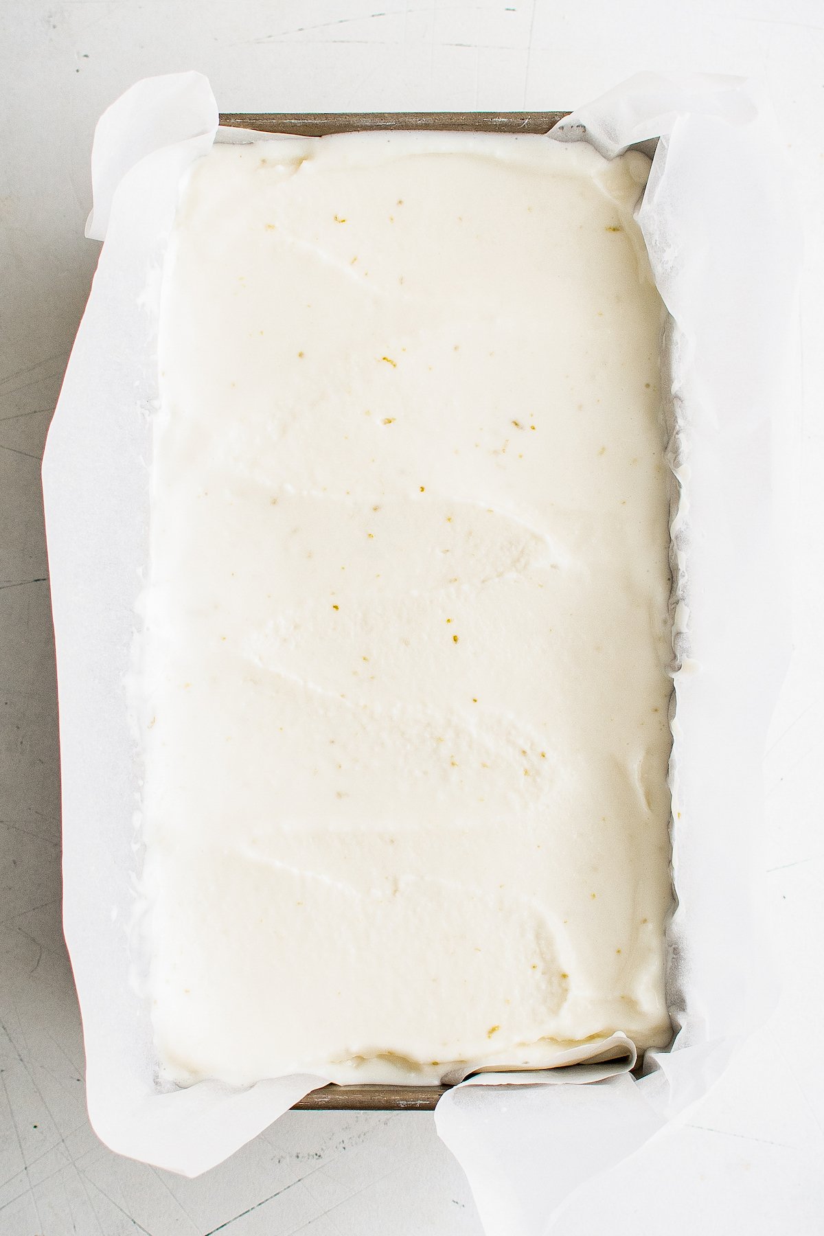 A shallow rectangular baking dish, lined with parchment and filled with soft frozen yogurt.