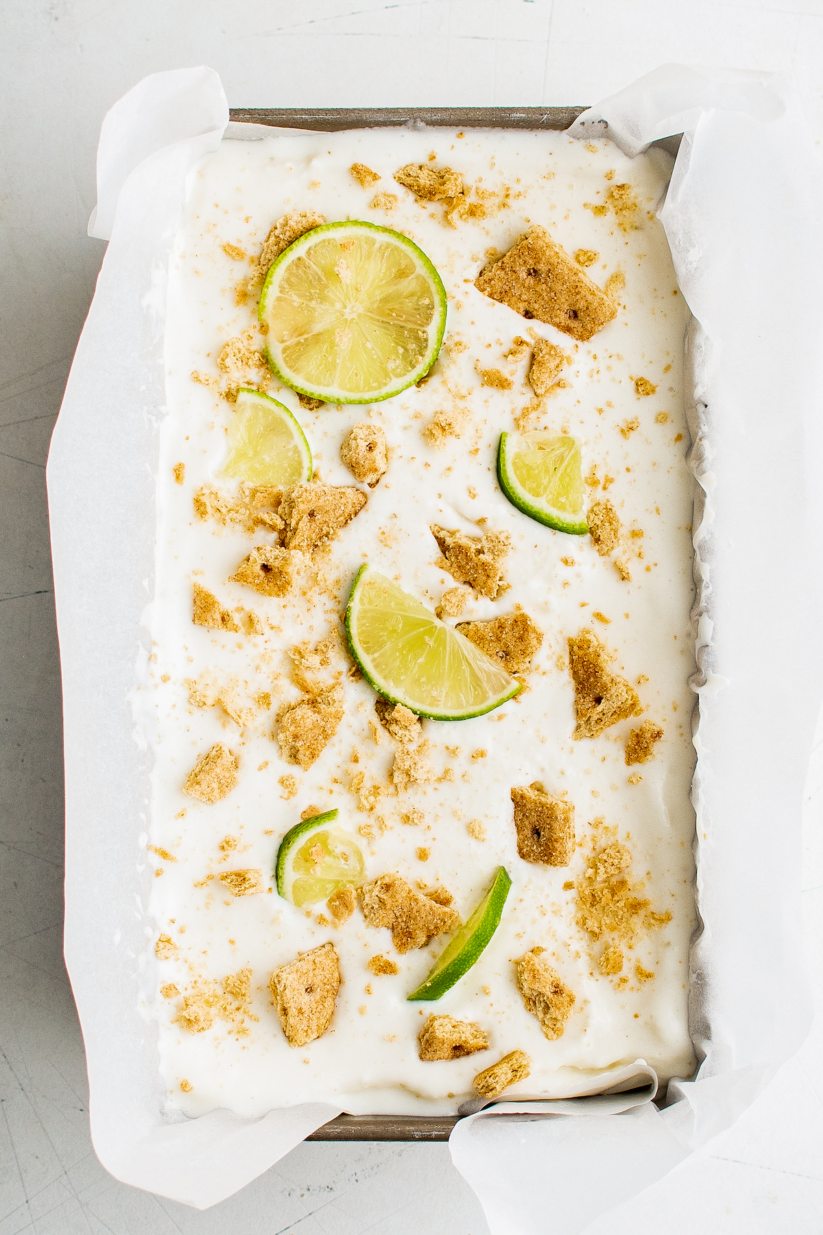 A shallow pan of key lime pie frozen yogurt, decorated with graham cracker crumbs and lime slices.