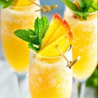 Up close image of peach bellini with fresh peaches and mint on top.