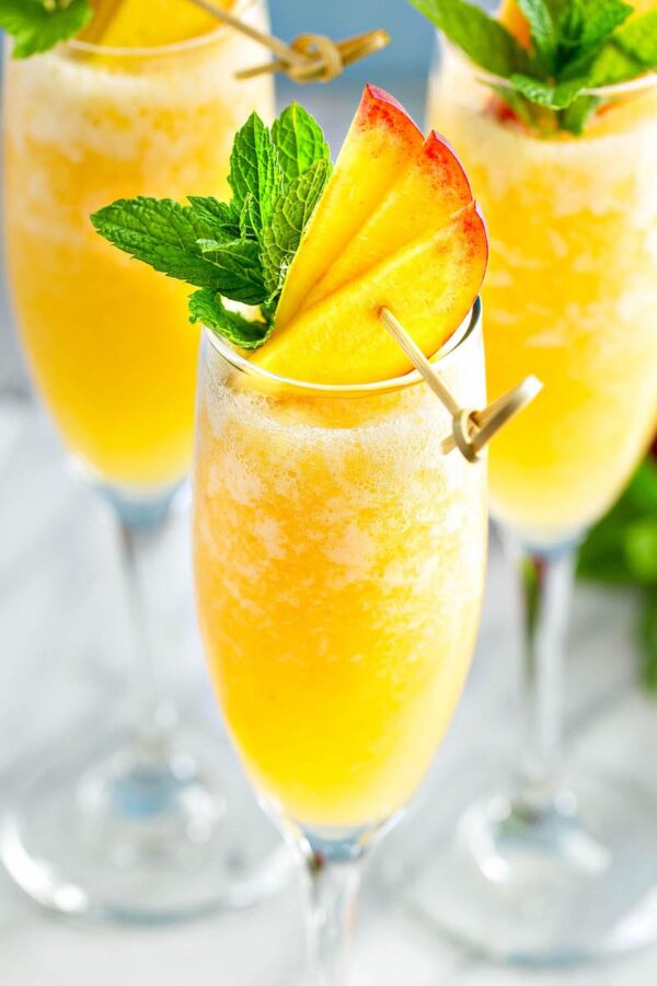 Peach Bellini in a glass with fresh peaches and mint on top. 